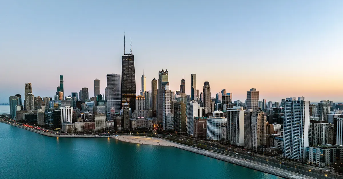 Panoramic high-angle view of the Chicago skyline at twilight, featuring the John Hancock Center and prominent skyscrapers along the Lake Michigan shoreline and Oak Street Beach.