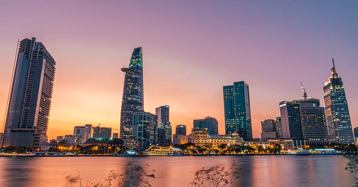 Ho Chi Minh City skyline at sunset showcasing District 1 illuminated skyscrapers, including the Bitexco Financial Tower, viewed across the Saigon River.