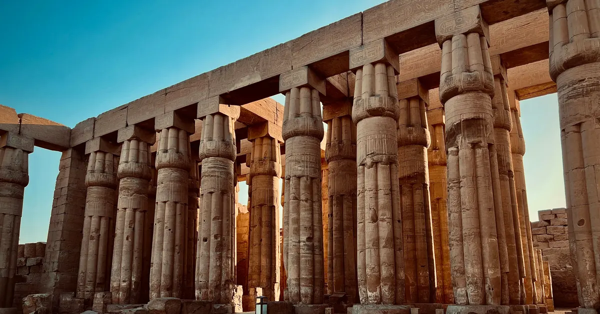 Stone pillars and architraves of the Court of Amenhotep III at Luxor Temple, Egypt, captured in profile under a clear sky.