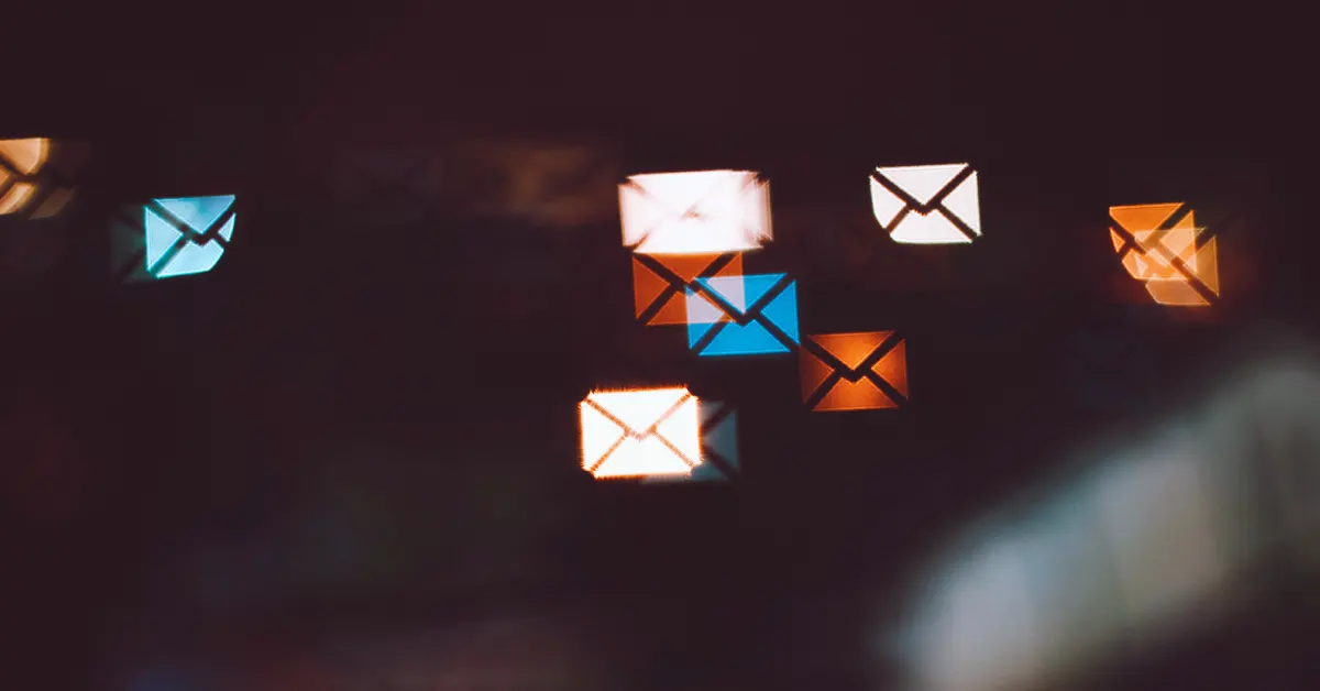 Abstract bokeh photography showing a cluster of glowing light artifacts shaped like mail envelope icons in white, blue, and orange against a dark background.