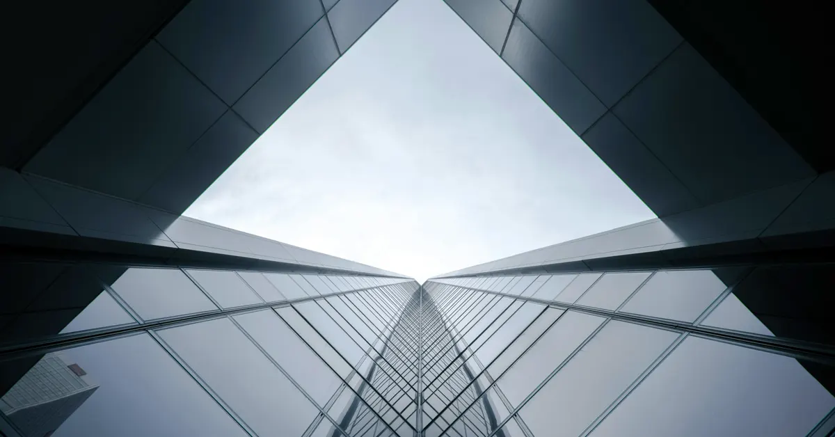 Low-angle view looking up at modern glass skyscrapers converging into a narrow triangular peak against the sky, symbolizing market consolidation and narrowing strategic choices.