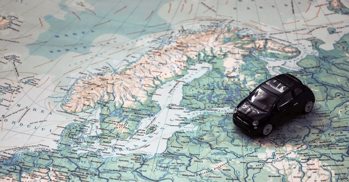 A small black toy car placed on a detailed paper map of Europe pointing across international borders.
