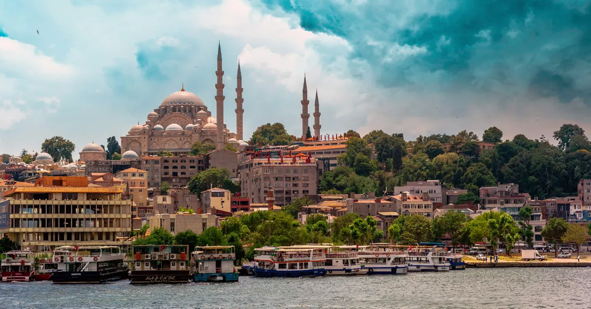 Panoramic view of the Istanbul skyline featuring the Süleymaniye Mosque on a hill above boats docked along the waterfront.