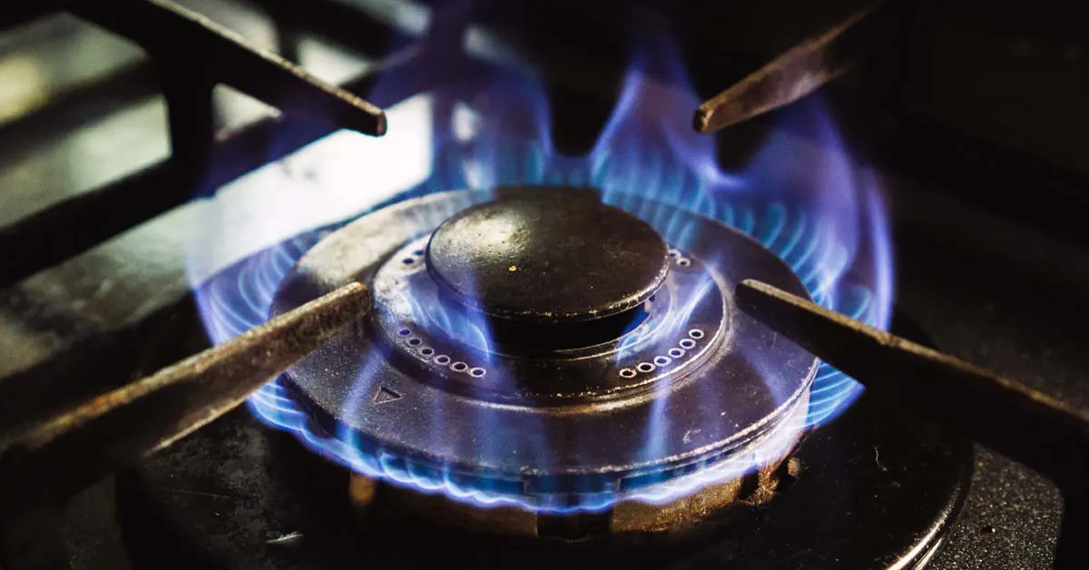 Close-up of a lit gas stove burner with bright blue flames emitting from the circular burner cap under a cast iron grate.