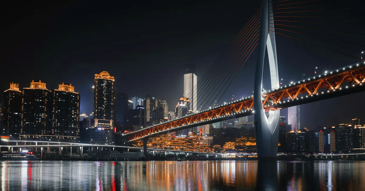 Illuminated Qiansimen Bridge spanning the river at night with the Chongqing city skyline and Hongyadong in the background.