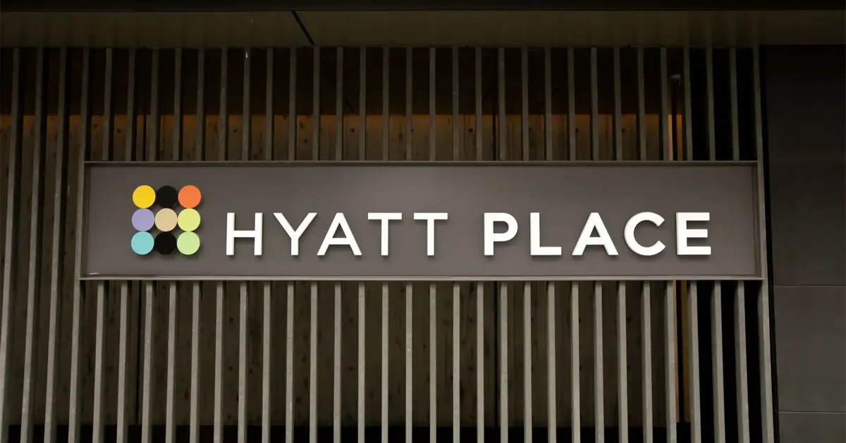 A horizontal sign displaying the illuminated "HYATT PLACE" logo alongside a grid of nine colorful circles against a dark wooden slatted wall.